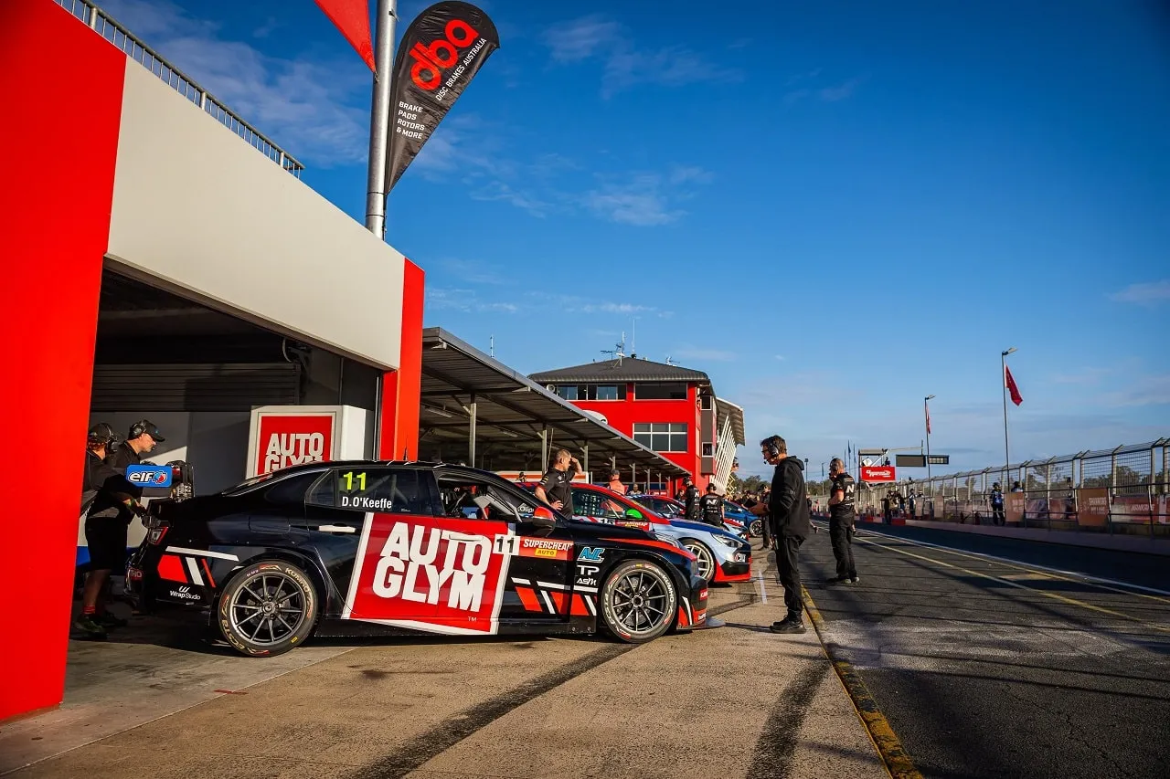 Black number 11 Autoglym Lynk & Co TCR car in a garage bay with crew members standing in pit lane