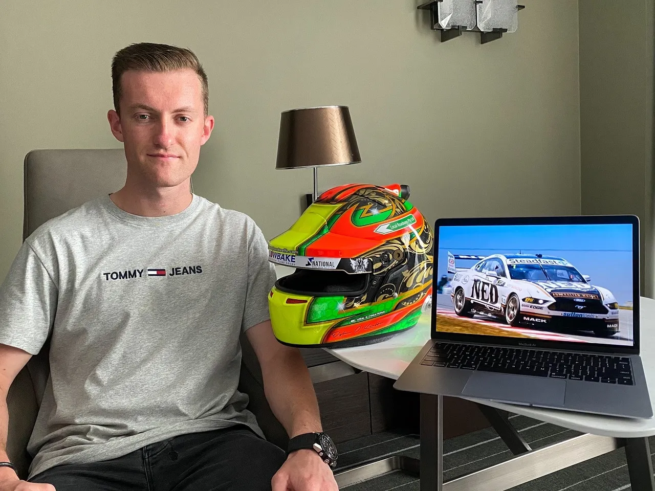 Dylan O’Keeffe seated in a hotel room next to his helmet and a laptop showing the NED Whisky Mustang