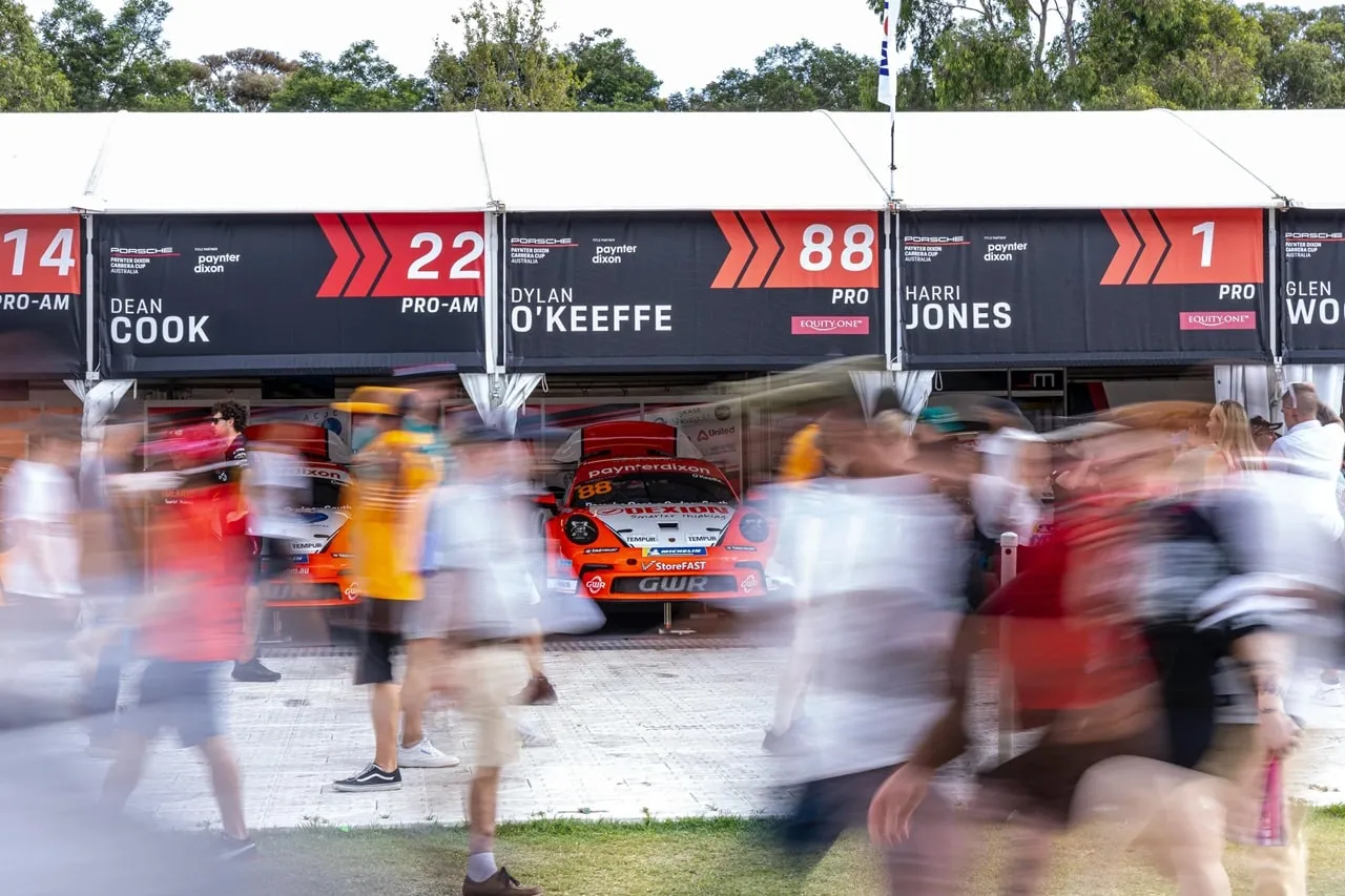 Blurred crowd walking past pit garage boards for Dylan O’Keeffe, number 88, and other Carrera Cup drivers