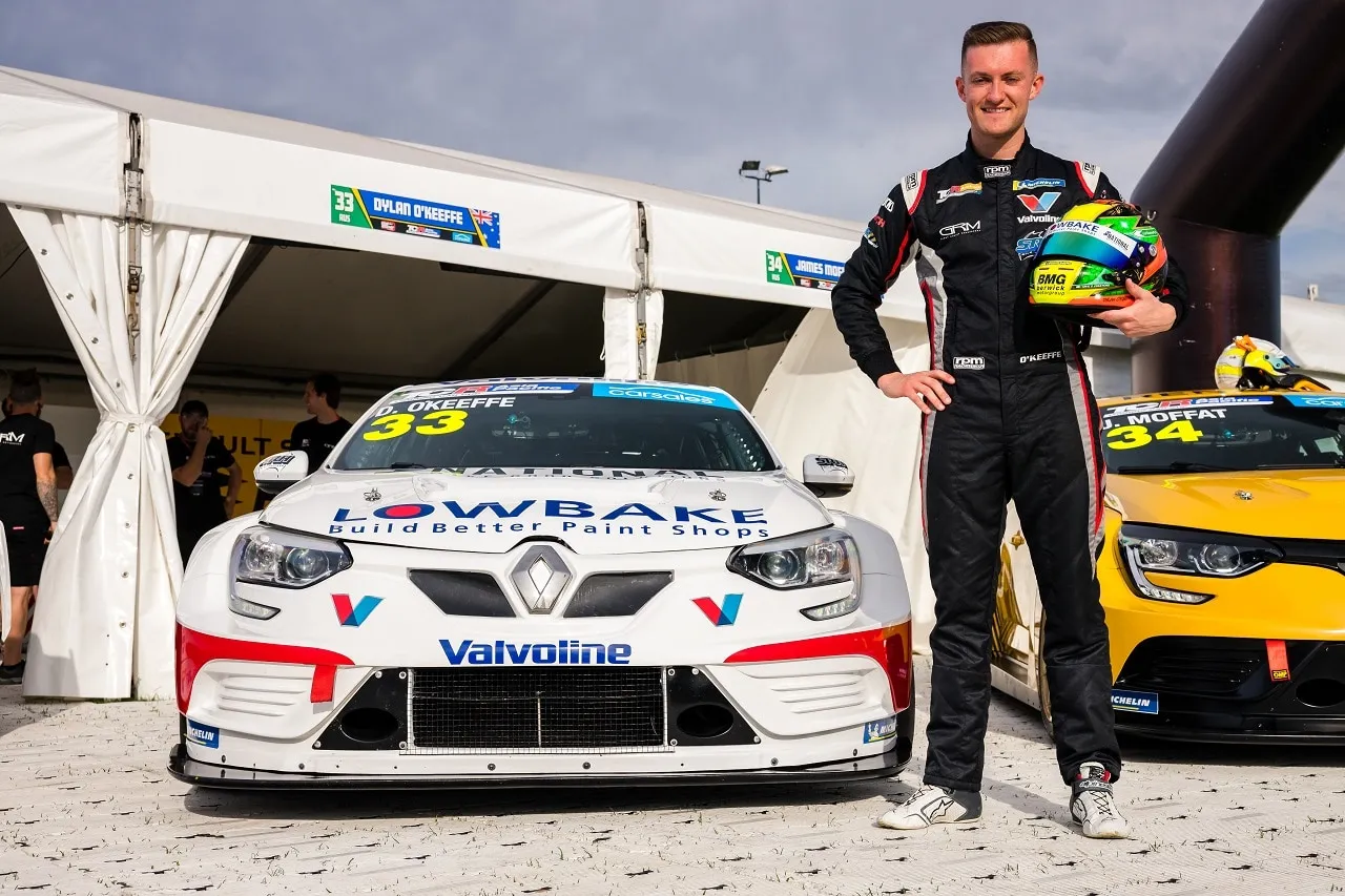 Dylan O’Keeffe standing in his race suit holding his helmet beside the white #33 Renault Megane RS TCR car
