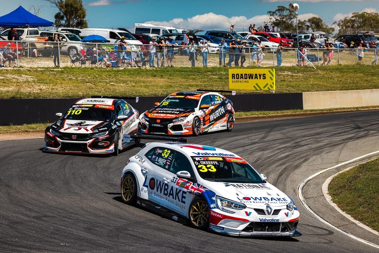 The #33 Renault Megane TCR car turning into a corner ahead of two other TCR cars, with spectators watching from the bank