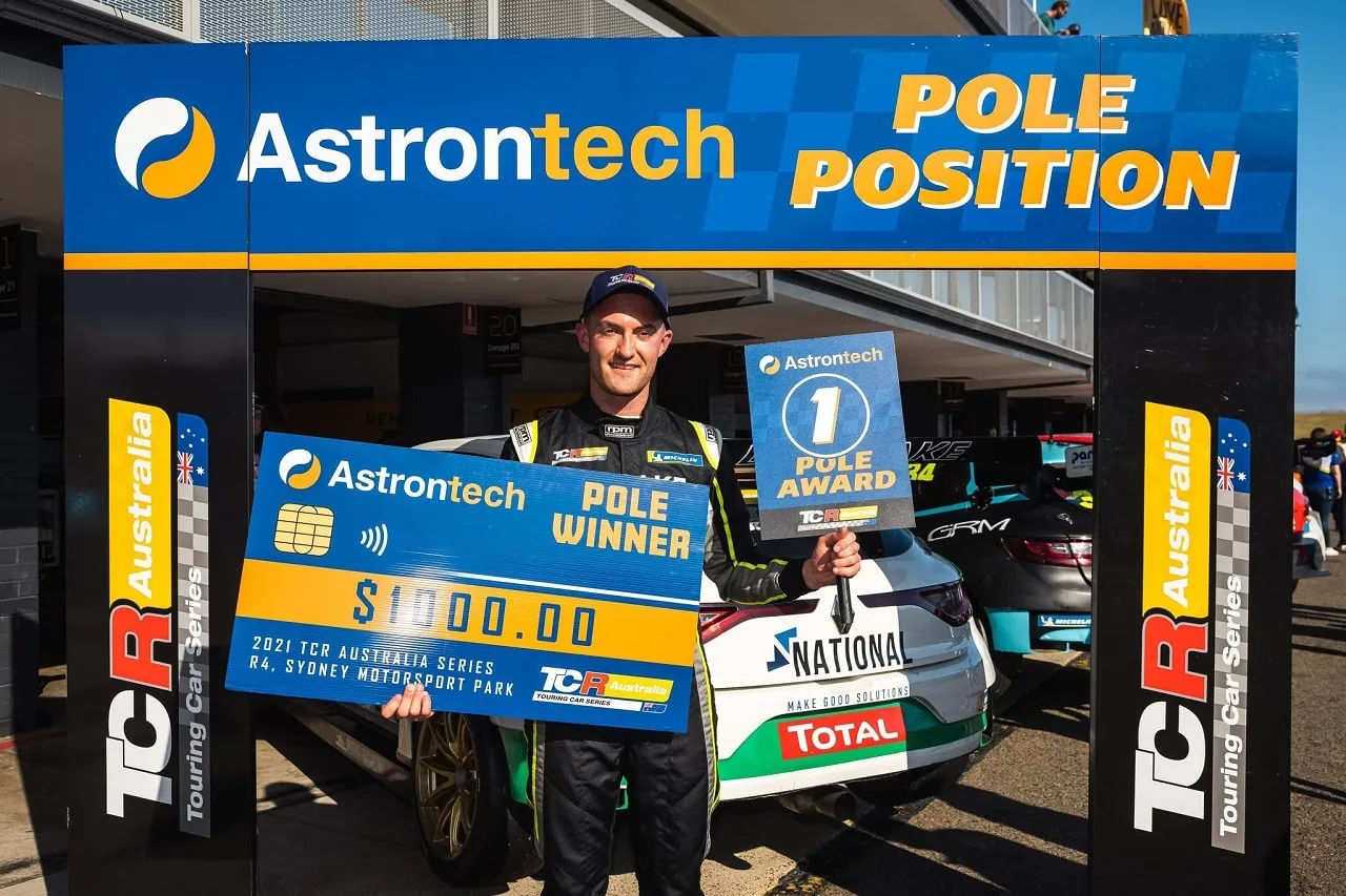 Dylan O’Keeffe holding a $1000 Pole Winner cheque and Pole Award sign under an Astrontech Pole Position gantry at Sydney Motorsport Park