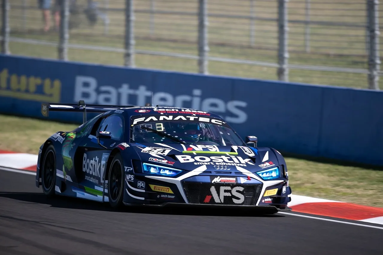 The dark blue Bostik AFS Audi R8 GT3 car on track past a Batteries sponsor barrier