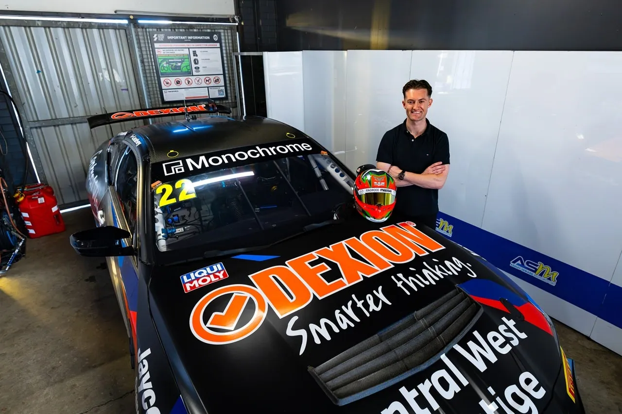 Dylan O’Keeffe standing arms folded beside a Dexion-liveried race car in the garage