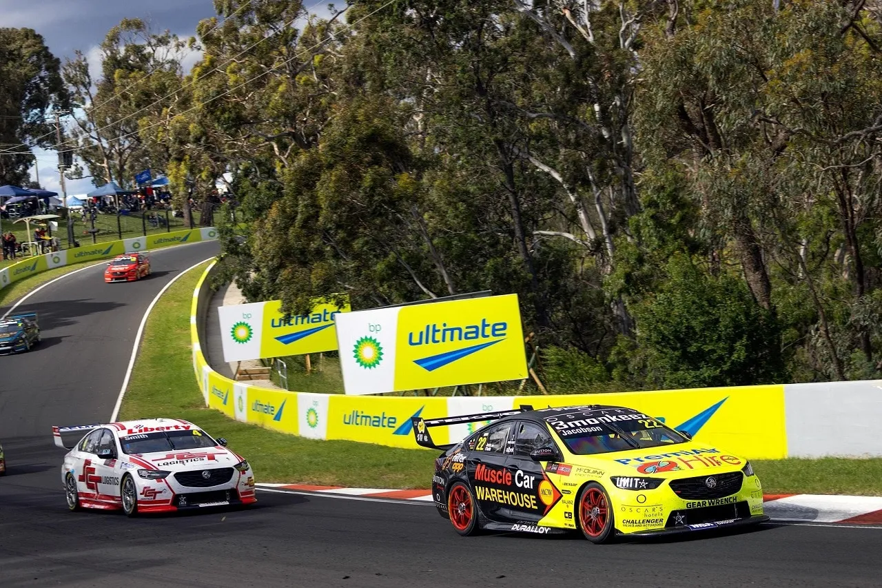 The yellow and black #22 PremiAir Hire Holden Commodore on track at Mount Panorama, Bathurst, with a red and white Commodore behind