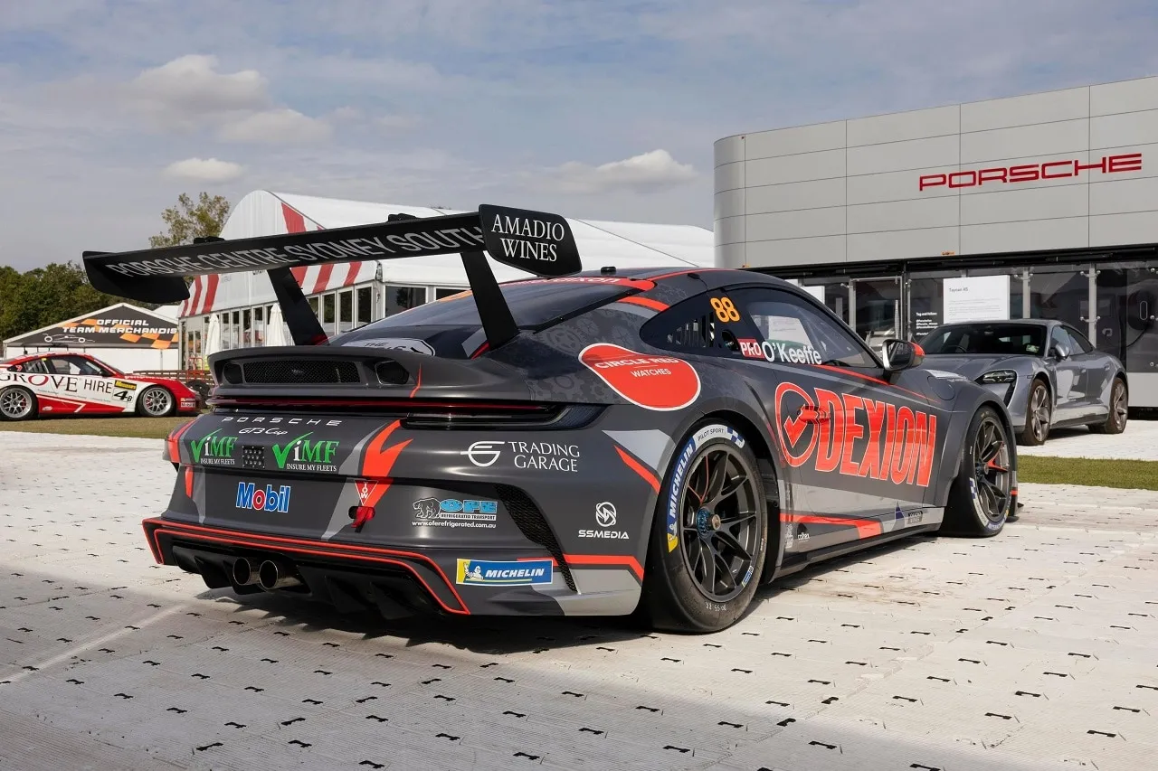 Rear three-quarter view of the #88 Dexion Porsche GT3 Cup car in the paddock with a Porsche Centre behind