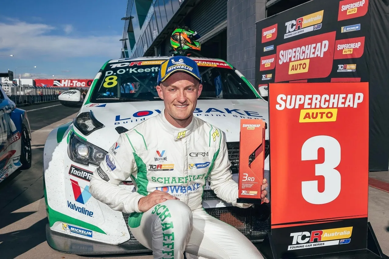 Dylan O’Keeffe kneeling with a third-place trophy beside a TCR Australia podium sign and his #8 Peugeot