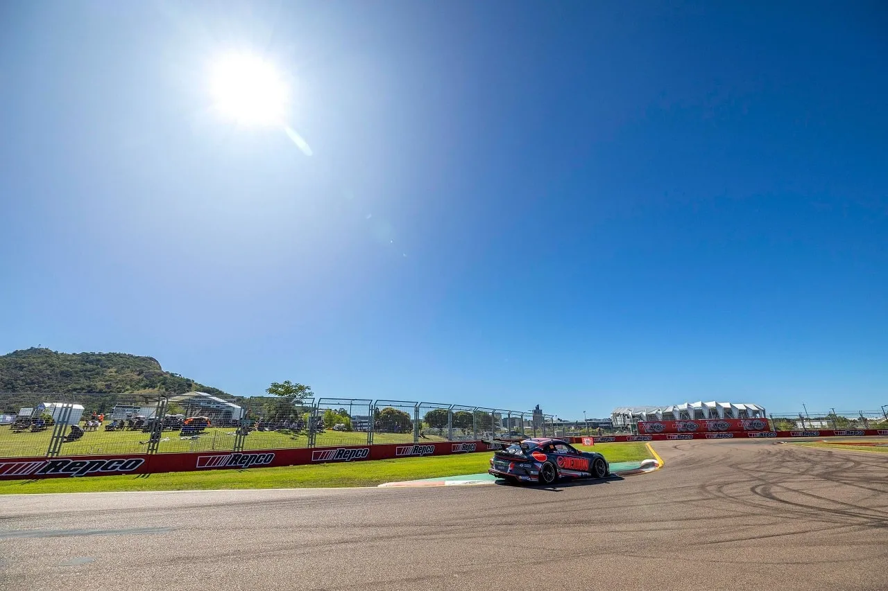 The #88 Porsche GT3 Cup car rounds a corner in the distance under a bright sun and deep blue sky