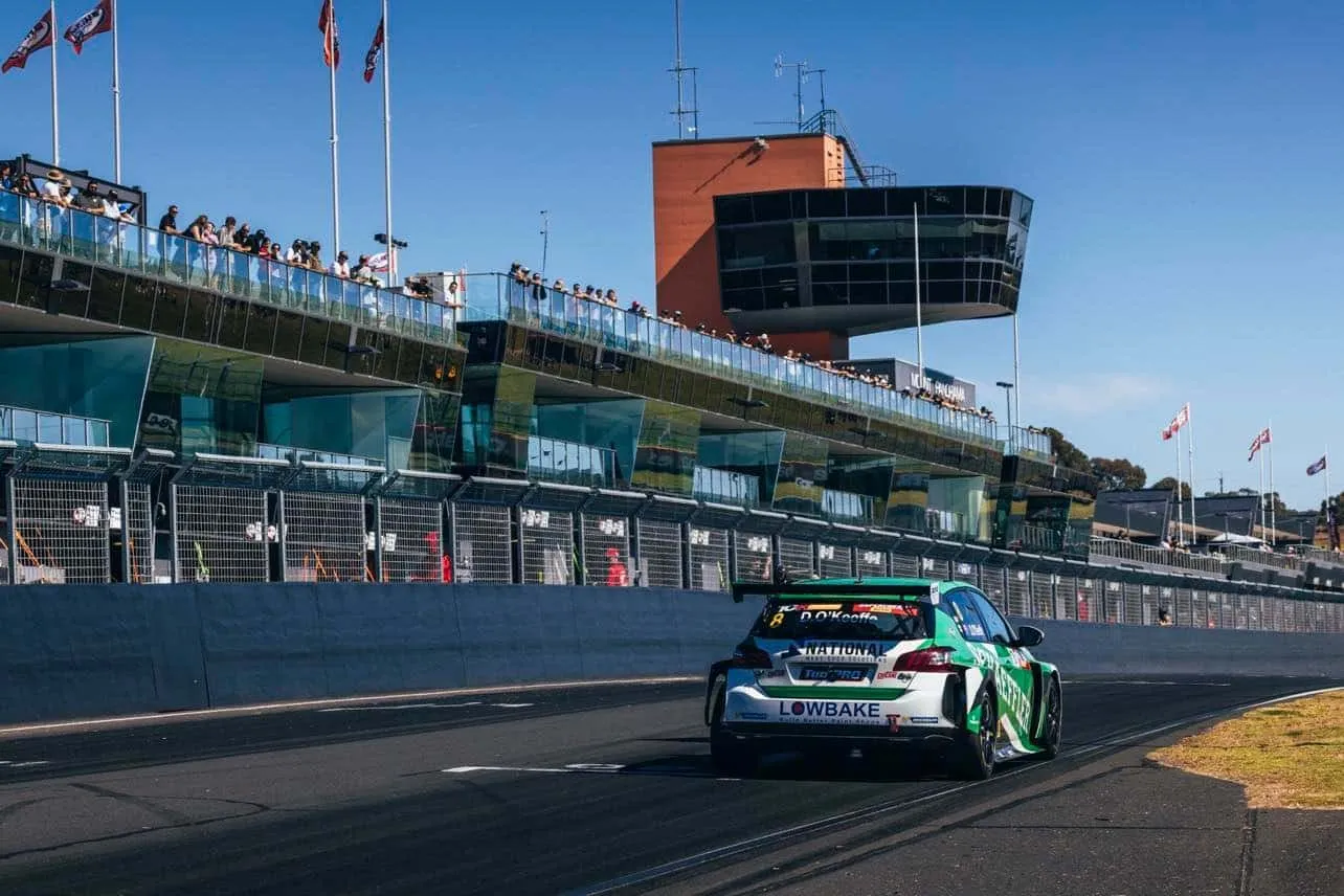 Rear view of the green and white Lowbake Peugeot 308 TCR car on track at Sandown in front of the grandstand