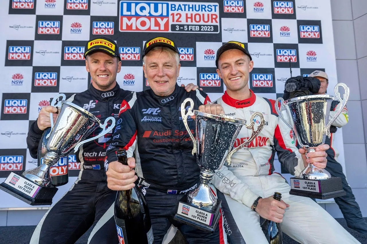 Three men on the Bathurst 12 Hour podium holding Class and Silver first place trophies, in front of a Liqui-Moly backdrop