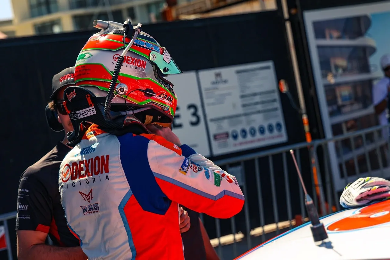 Driver in a Dexion Victoria race suit and helmet embracing a team member beside a race car