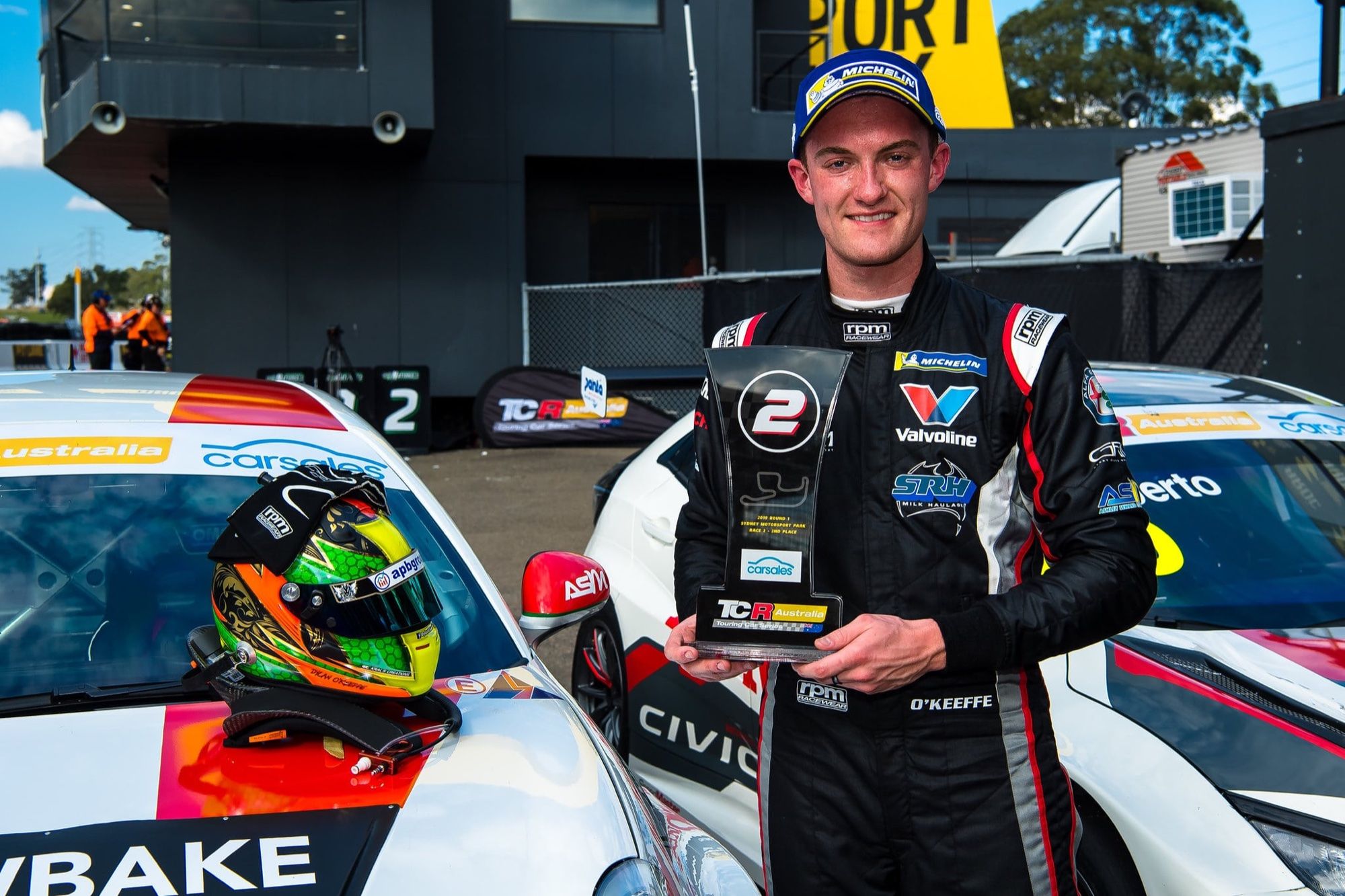 Dylan O’Keeffe holding a second-place TCR Australia trophy beside his helmet on the roof of his Alfa Romeo