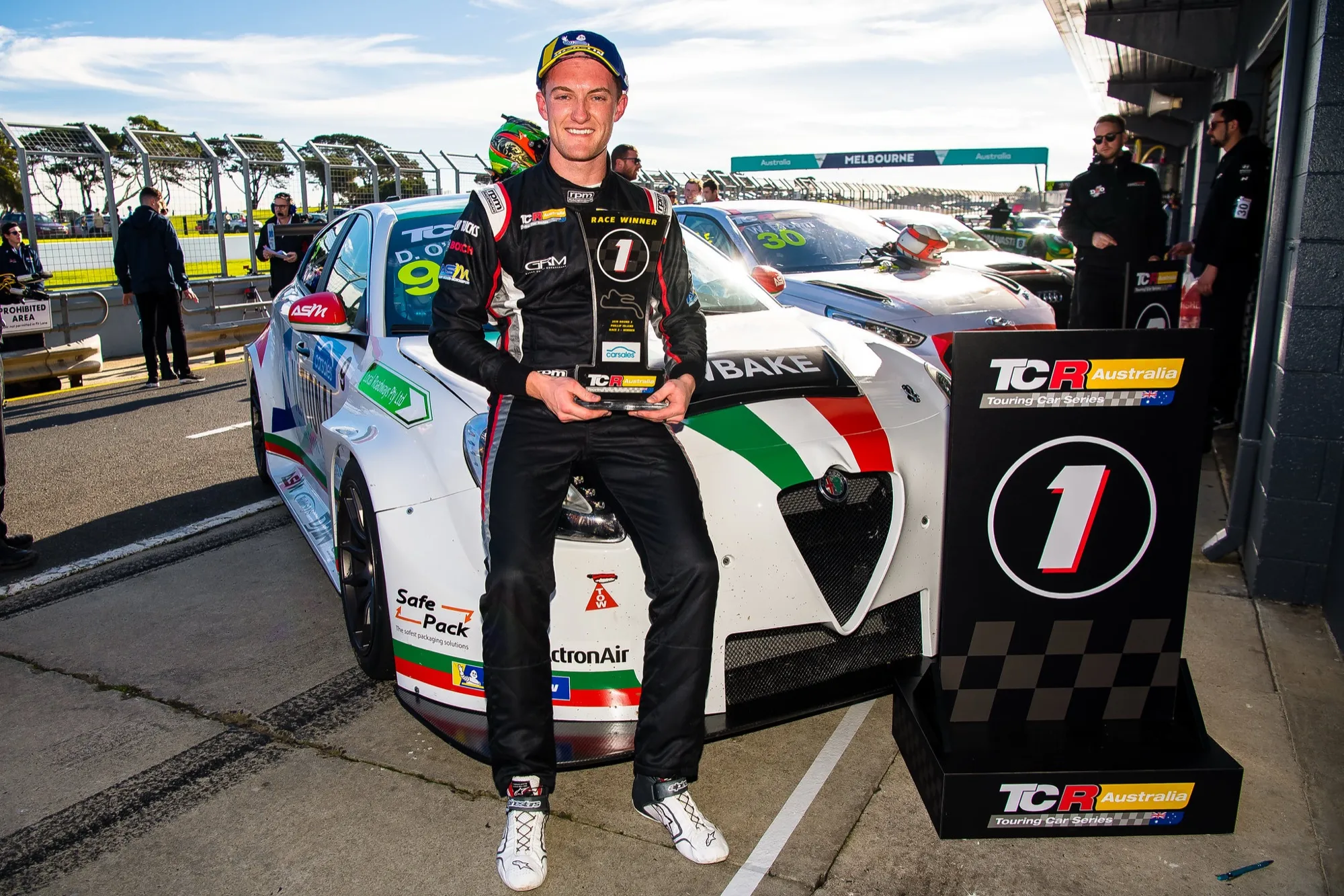 Dylan O’Keeffe sitting on his #9 Alfa Romeo TCR car holding a TCR Australia race winner trophy