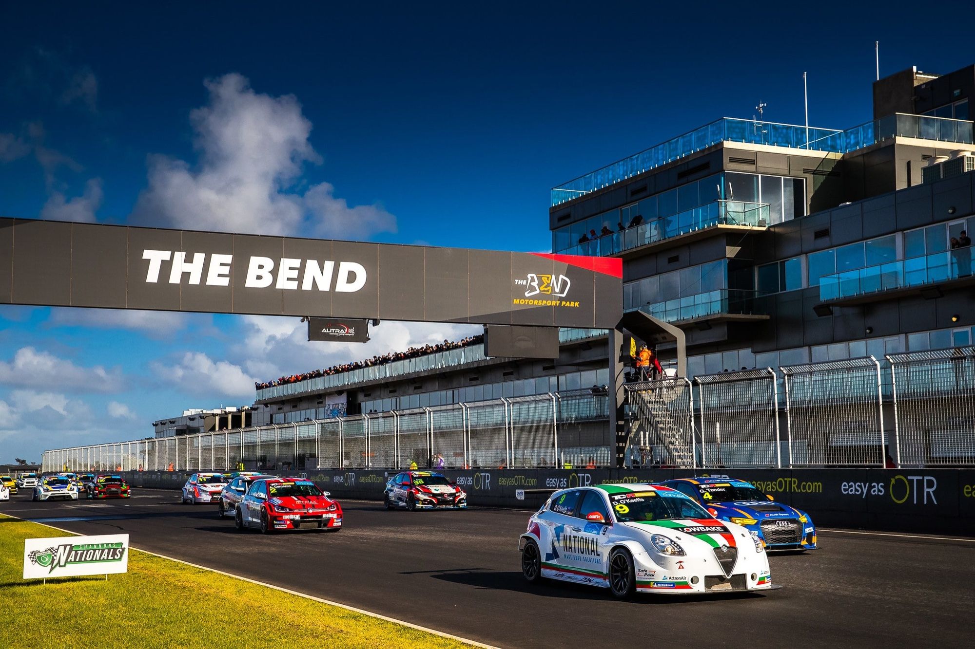 The white #9 Alfa Romeo TCR car in a group of cars at the start beneath The Bend Motorsport Park gantry
