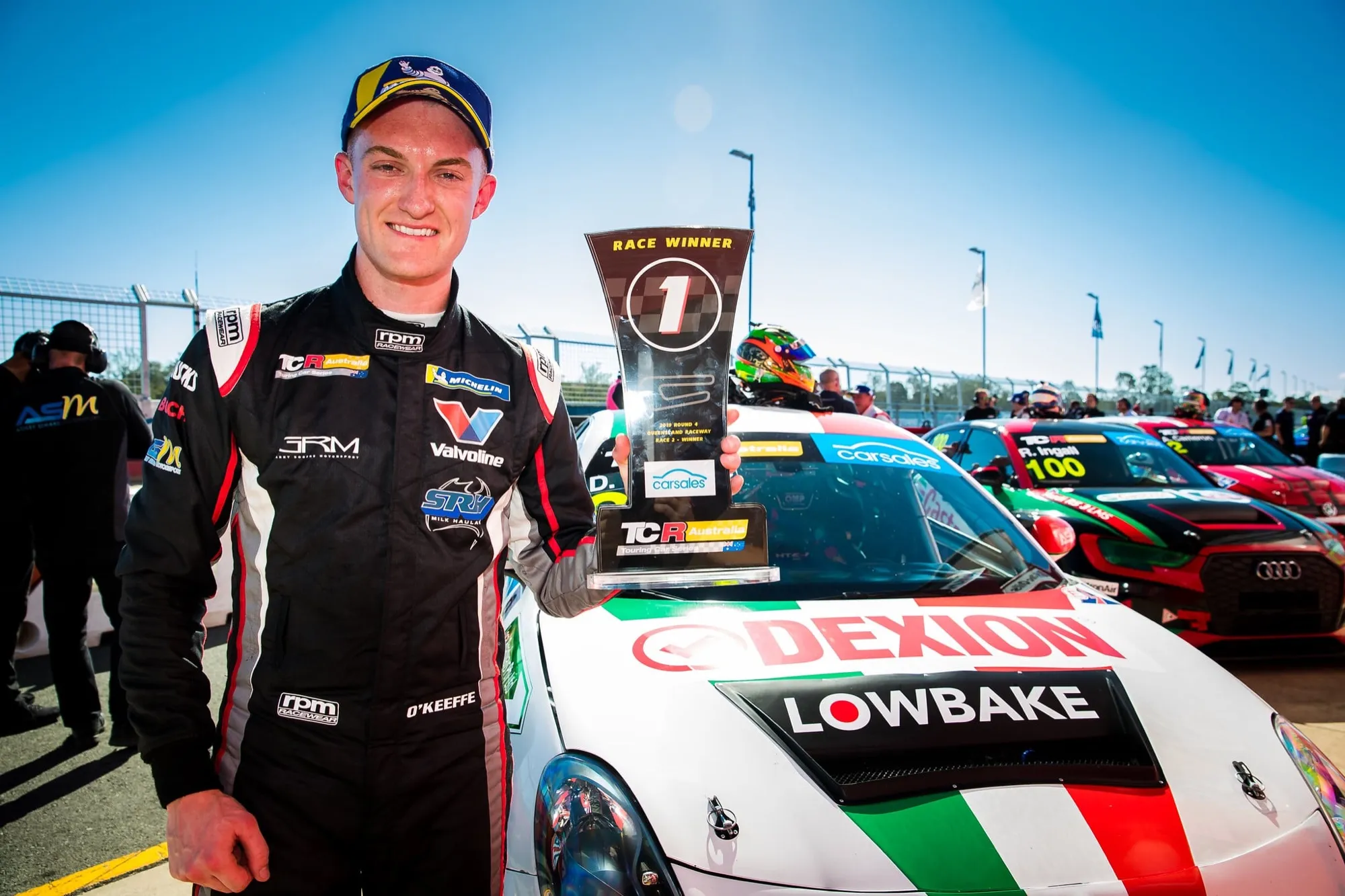 Dylan O’Keeffe holding a TCR Australia race winner trophy in front of his Dexion Lowbake Alfa Romeo