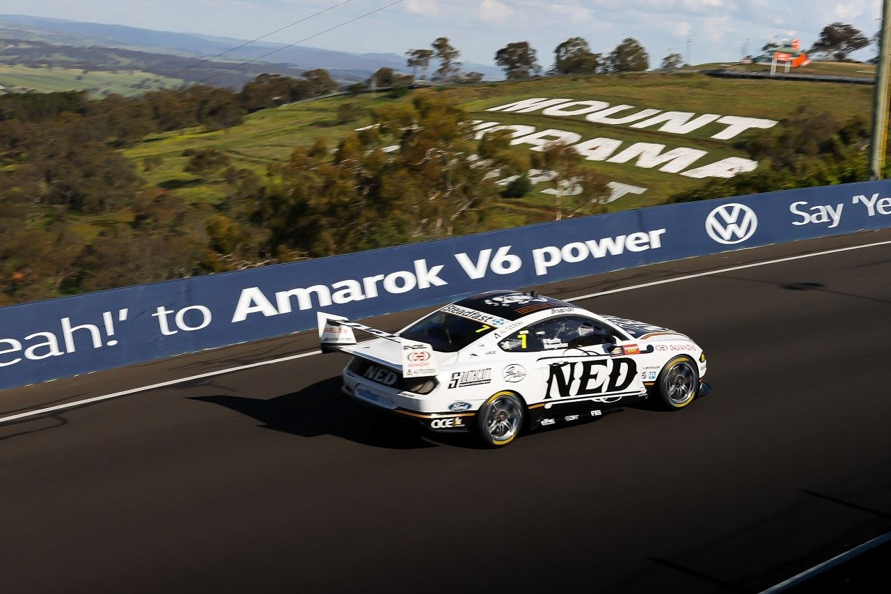 The white NED Whisky Ford Mustang Supercar on track at Mount Panorama beside an Amarok V6 barrier sign