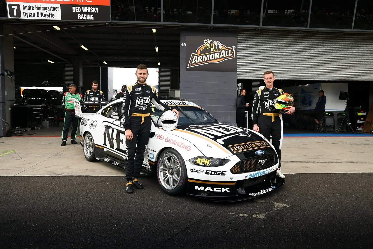 Two drivers in NED Whisky Racing suits stand beside the NED Ford Mustang Supercar, with a sign reading Andre Heimgartner and Dylan O’Keeffe