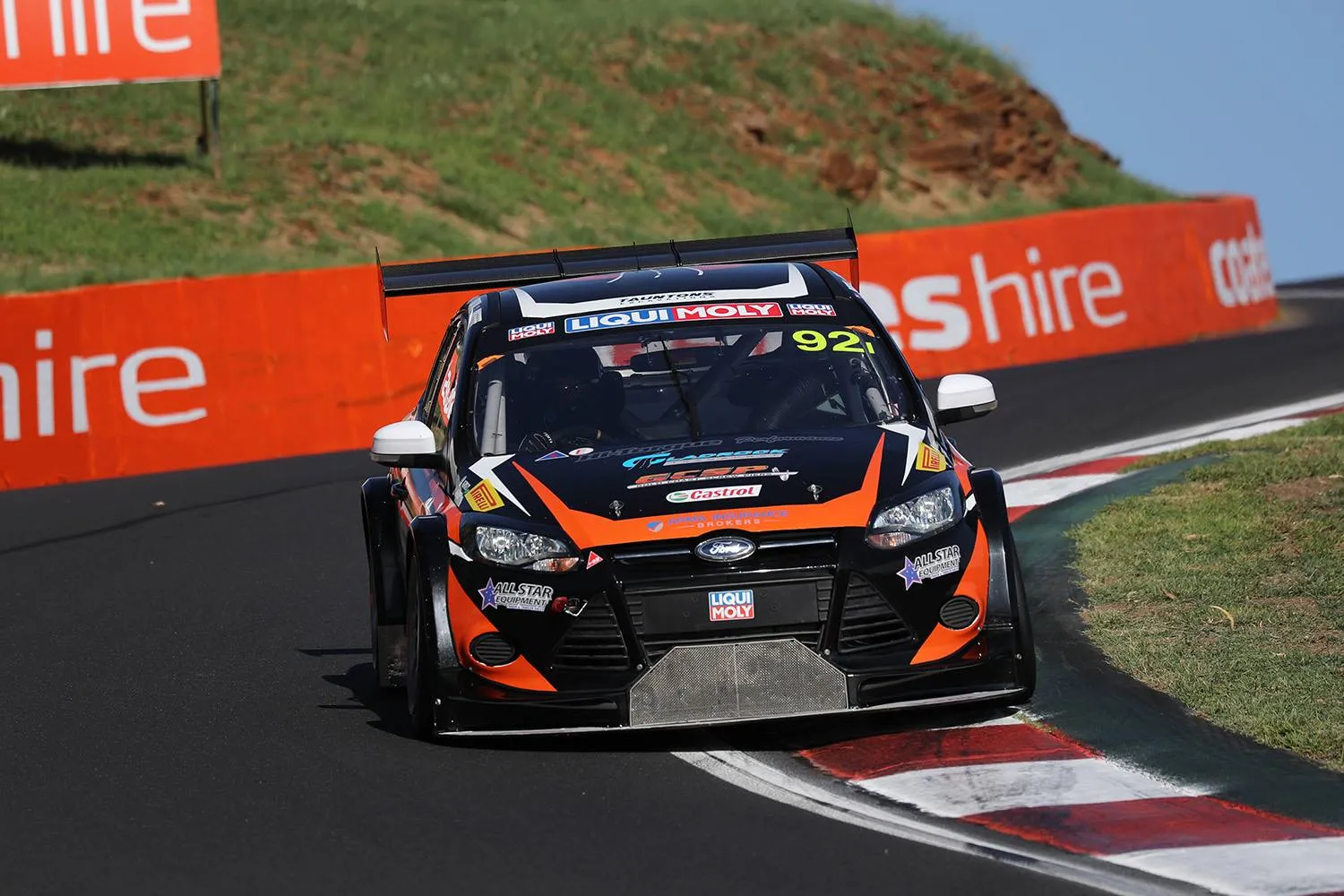 The black and orange #92 MARC Ford Focus racing at speed beside orange Coates Hire barriers at Mount Panorama