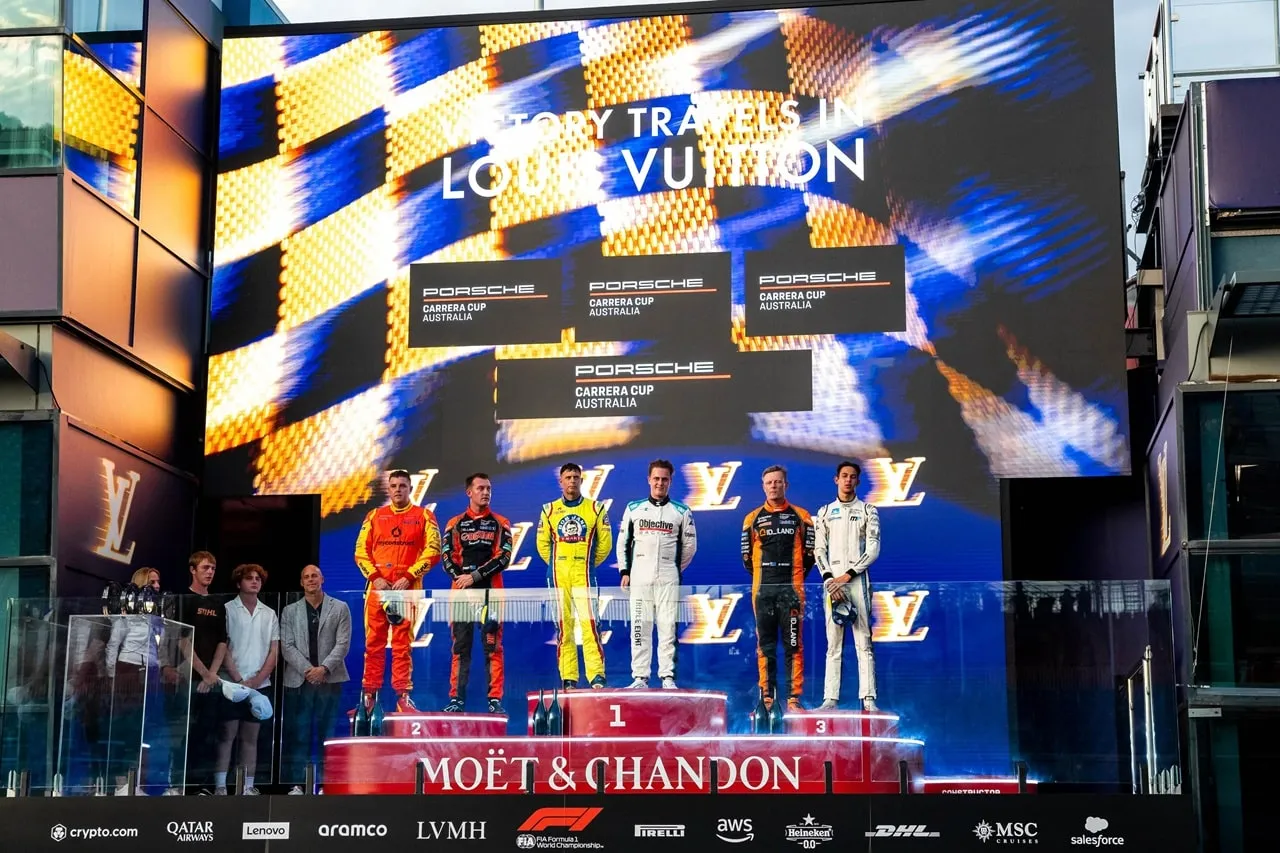 Drivers on the podium in front of a large screen reading Victory travels in Louis Vuitton