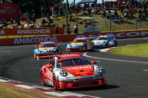 Dylan O’Keeffe’s #1 Dexion Porsche leading a pack of Carrera Cup cars at Bathurst, spectators on the hill behind the Anaconda banners