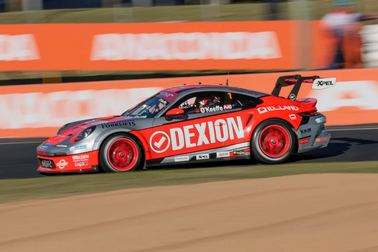 Dylan O’Keeffe’s orange and silver Dexion Porsche at speed past orange trackside banners at Bathurst