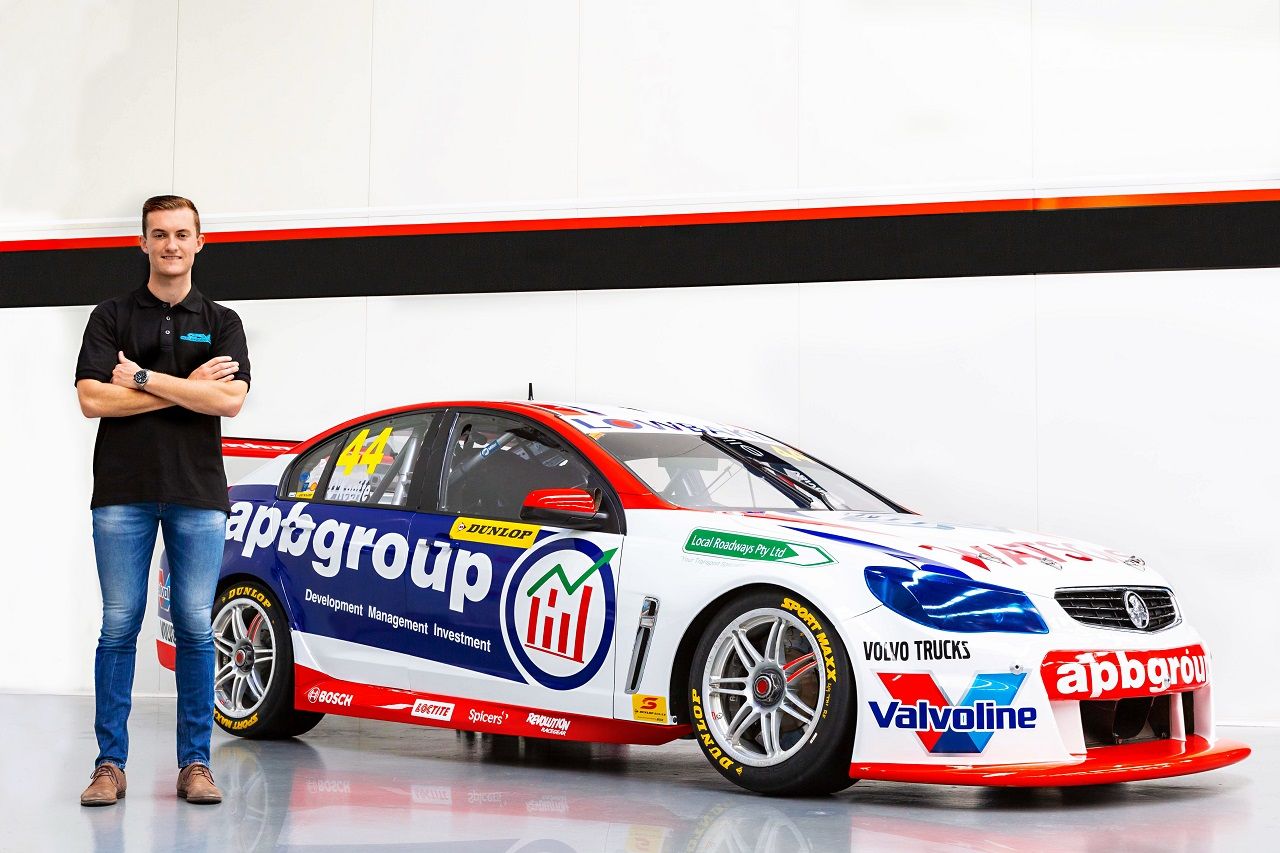 Dylan O’Keeffe standing with arms crossed beside the blue, white and red #44 apbgroup Commodore Supercar in a studio