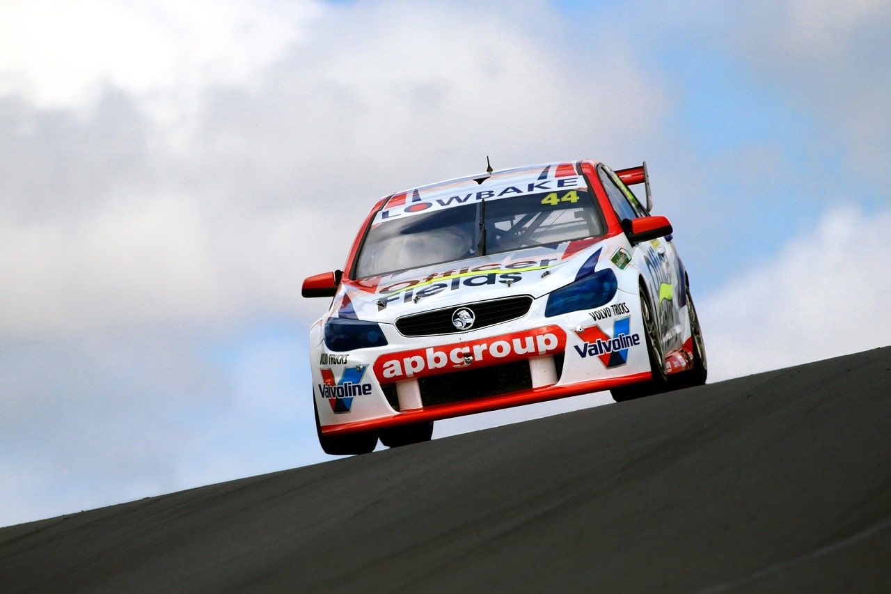 The #44 apbgroup Lowbake Commodore Supercar cresting a rise against a cloudy blue sky