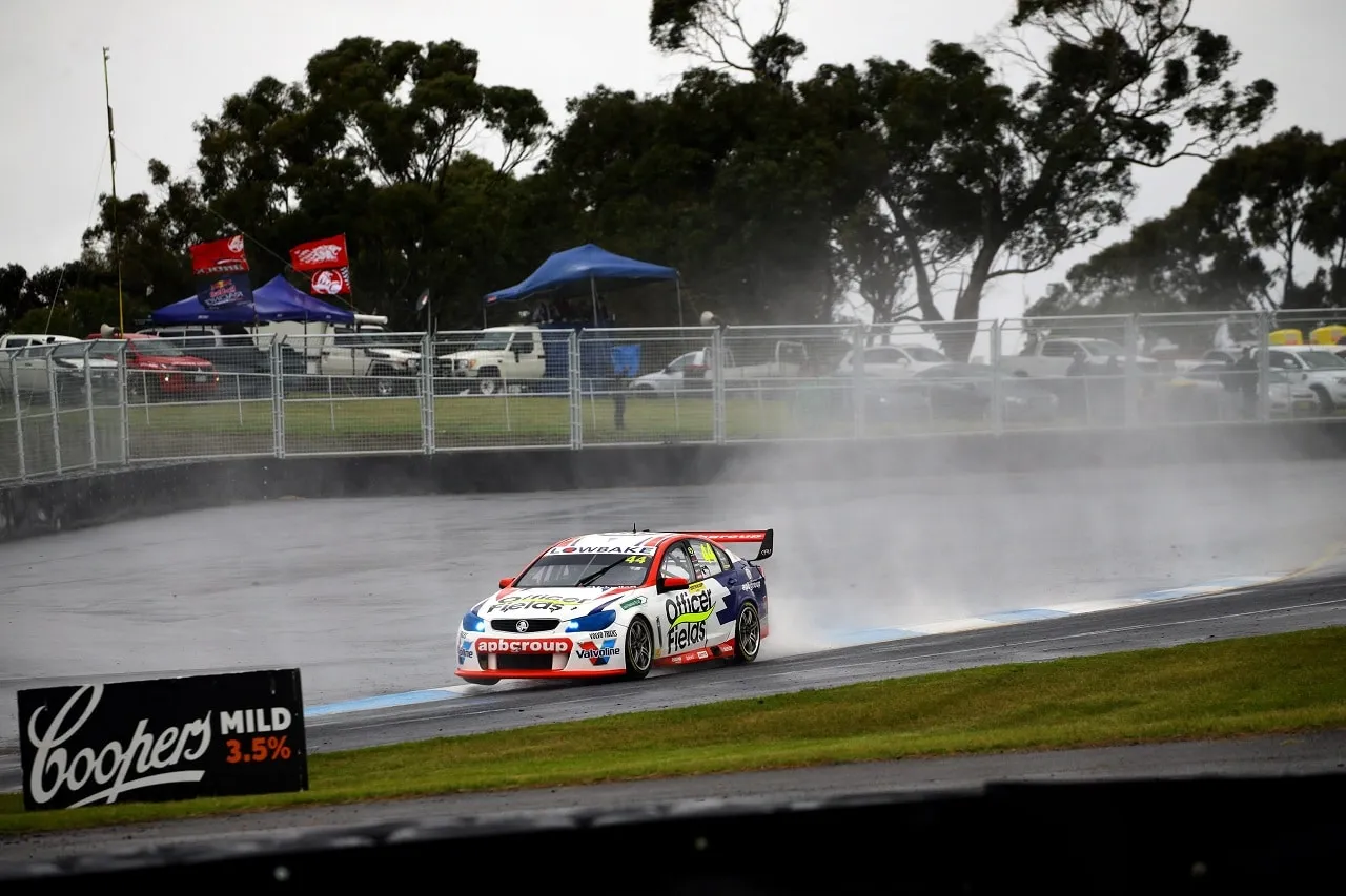 A Holden Commodore Supercar throws up spray on a wet track beneath grey skies