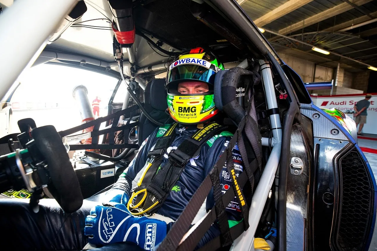 Driver in a Lowbake helmet strapped into the cockpit of the Bostik Audi R8 GT3 in the garage