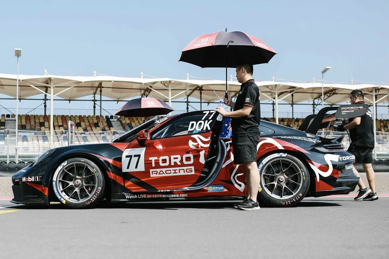 Toro Racing Porsche #77 in the pit lane with a crew member holding an umbrella by the door