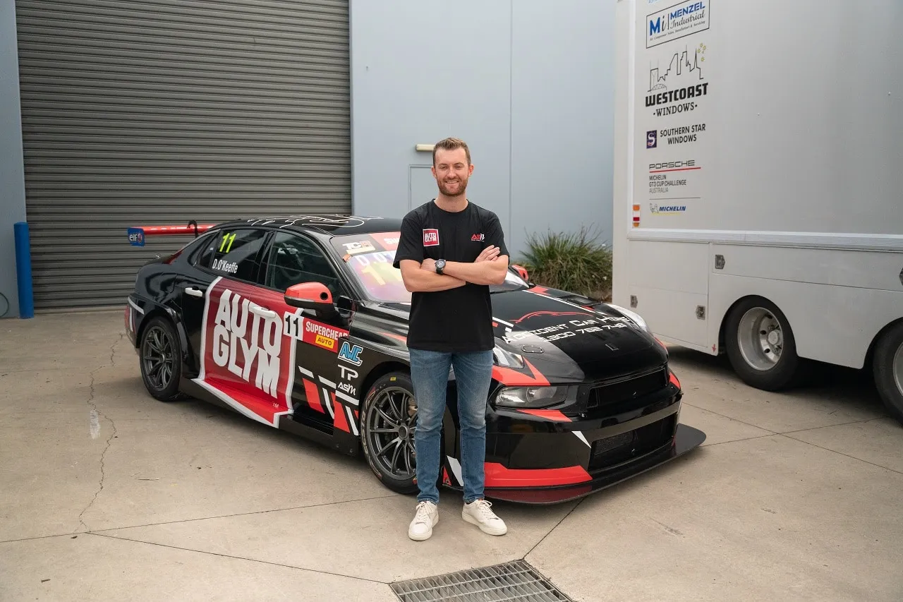 Dylan O’Keeffe with arms crossed beside his new black Autoglym Lynk & Co TCR car outside a workshop
