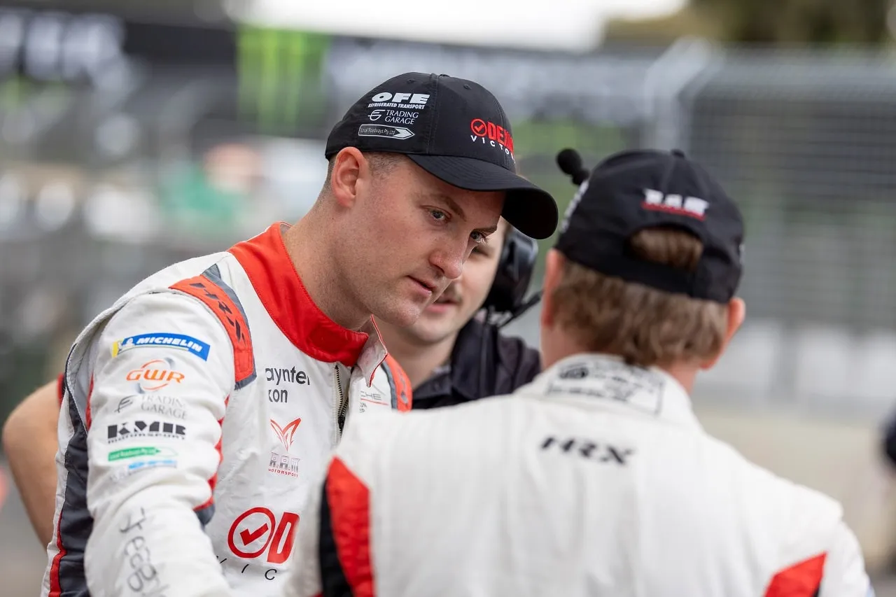 Dylan O’Keeffe in a Dexion Victoria race suit and cap talking with a team member in the pit lane