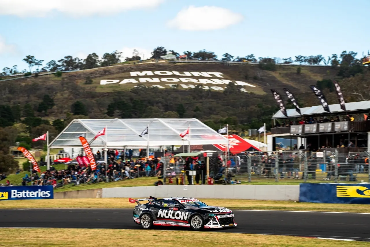 The black Nulon Camaro racing on track at Bathurst with the Mount Panorama sign on the hill behind