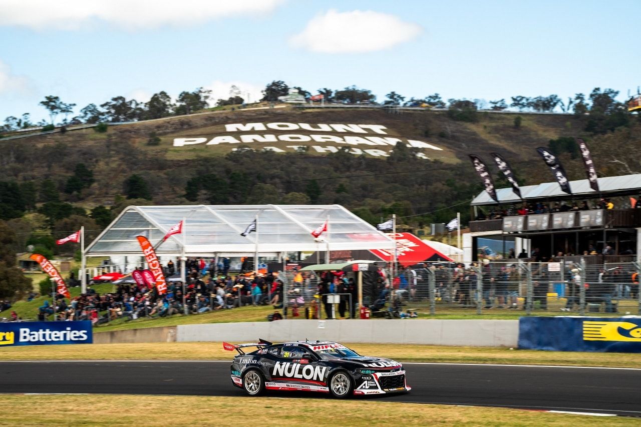The black Nulon Camaro racing on track at Bathurst with the Mount Panorama sign on the hill behind