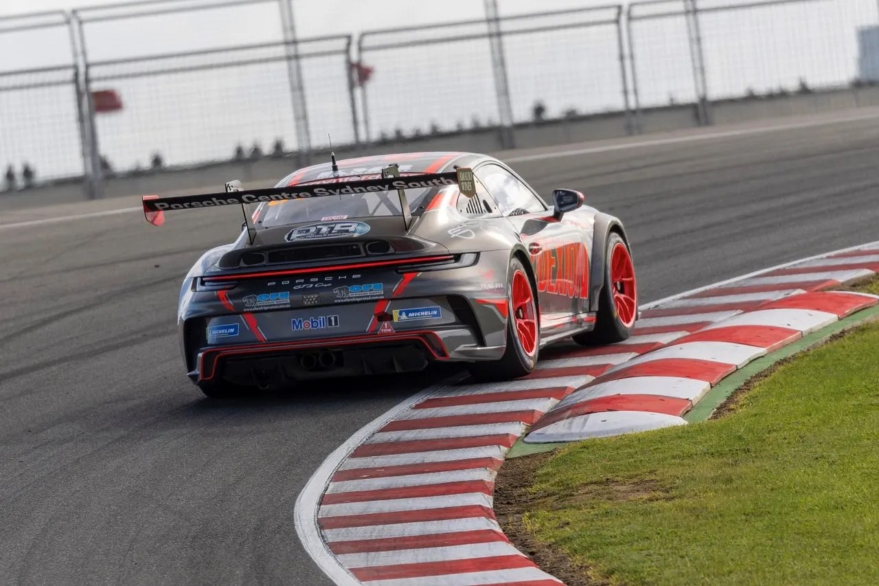 Rear three-quarter view of the grey Porsche 911 GT3 Cup car on a red and white kerbed corner