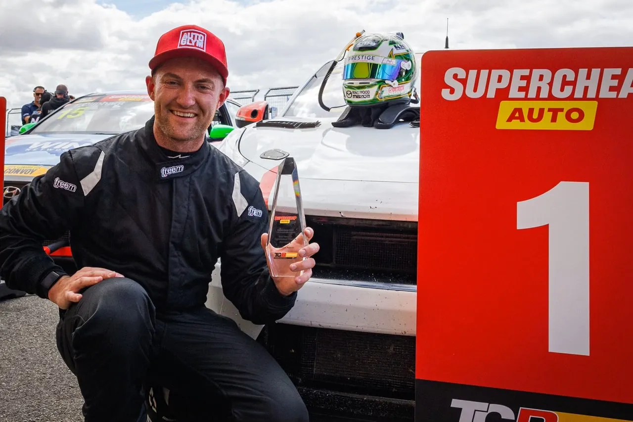Dylan O’Keeffe crouching with a trophy beside a Supercheap Auto number 1 winner’s sign