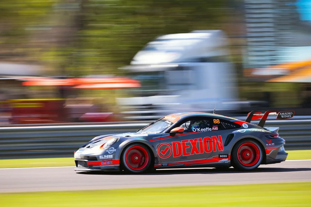 Side view of the number 88 Dexion Porsche 911 GT3 Cup car at speed with a blurred truck in the background