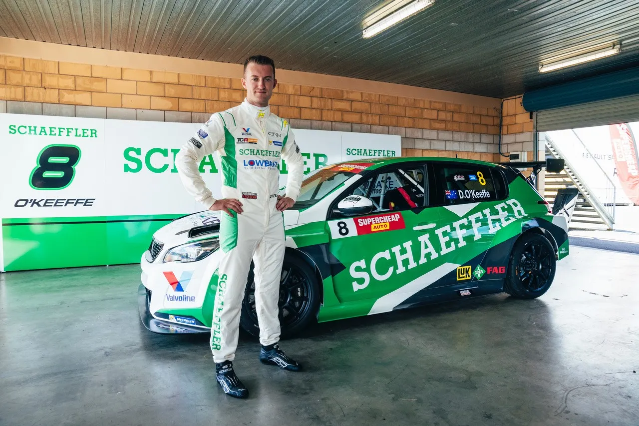Dylan O’Keeffe in a white Schaeffler race suit standing beside his #8 Peugeot 308 TCR car in the garage