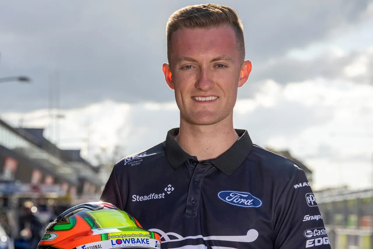 Dylan O’Keeffe smiling in a Ford team shirt with his race helmet in front of him in pit lane
