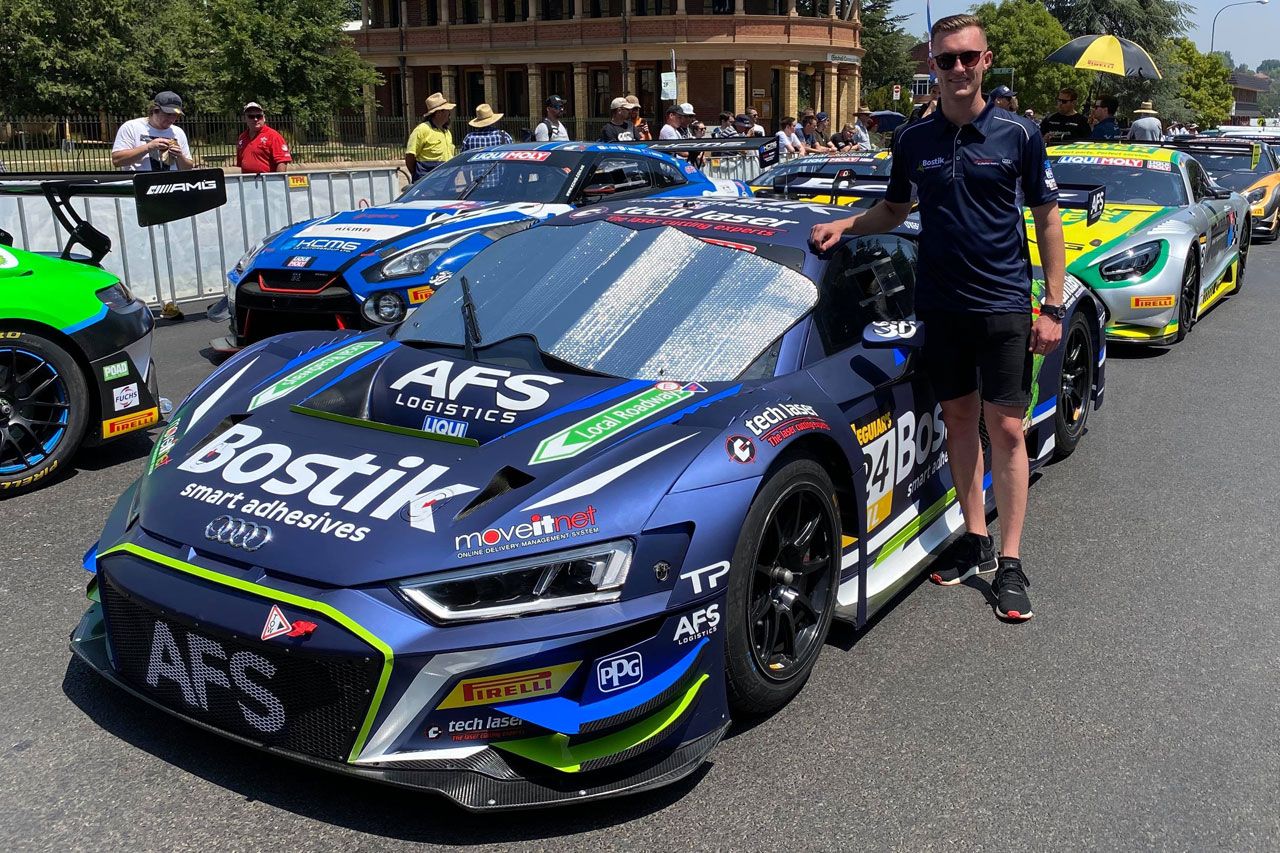 Dylan O’Keeffe standing beside the front of the blue Bostik AFS Audi R8 GT3 car in a street parade with other GT cars