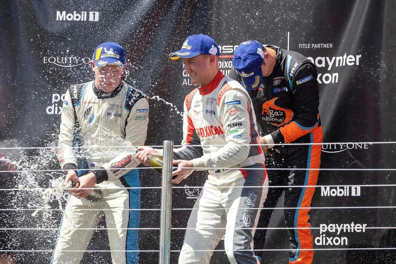 Three Carrera Cup drivers spraying champagne on the podium in front of a Paynter Dixon backdrop