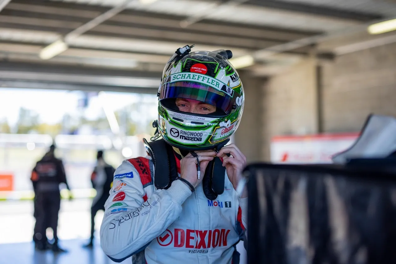 Dylan O’Keeffe in a green Schaeffler helmet and Dexion Victoria race suit adjusting his gear in the garage