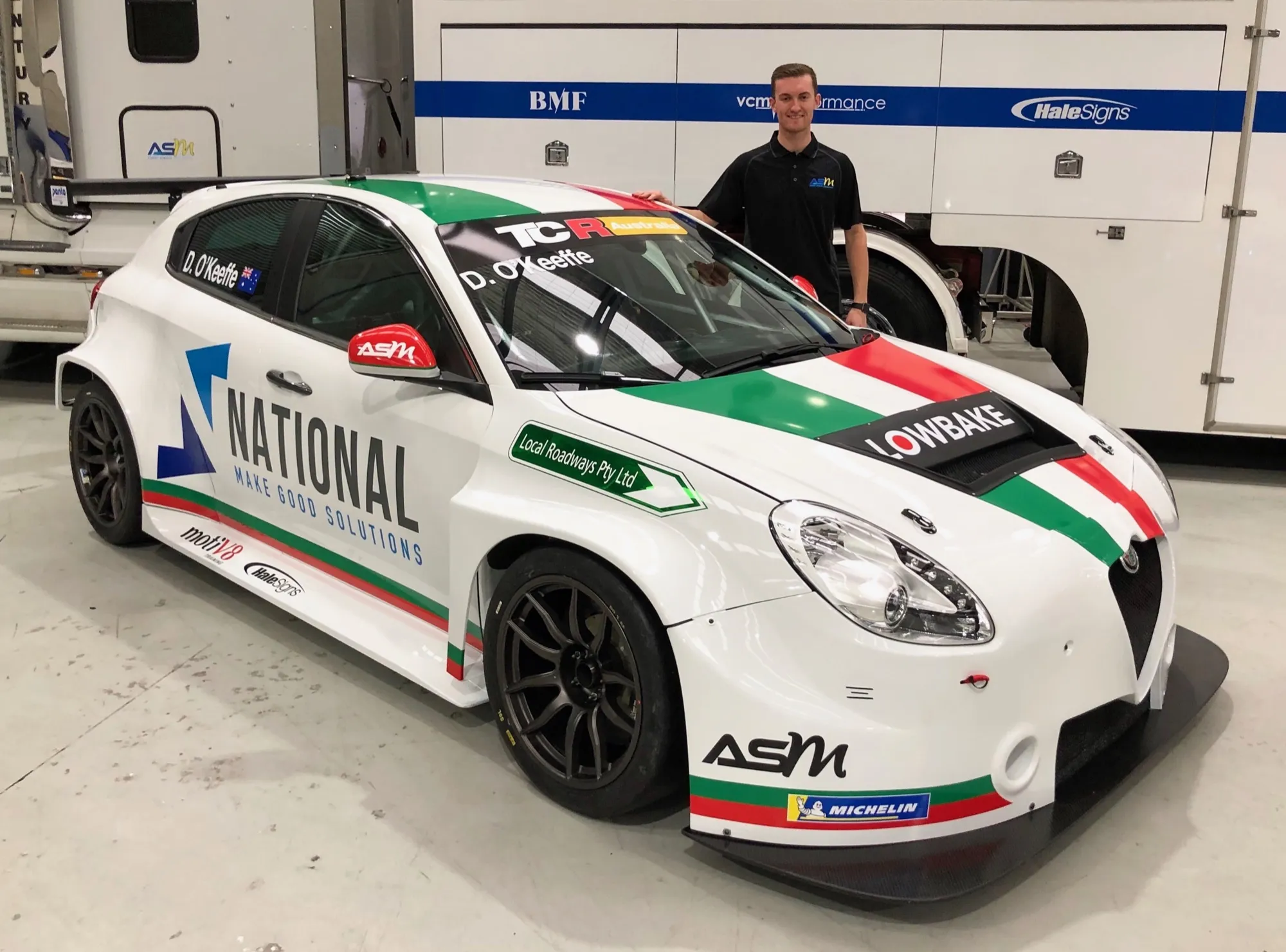 A team member stands beside the Italian-flag-inspired white Alfa Romeo Giulietta TCR car with National and Lowbake sponsors