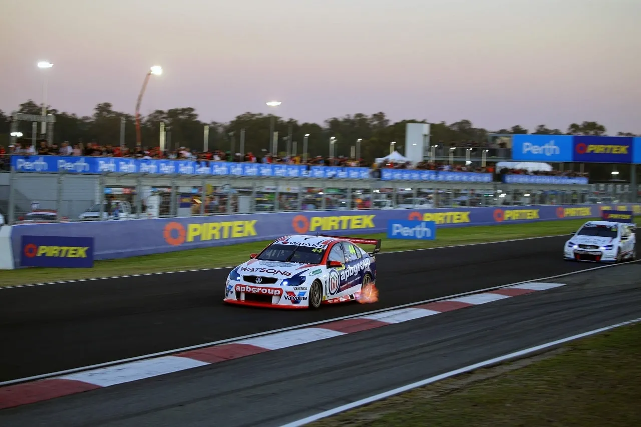 The #44 apbgroup Commodore Supercar at dusk under lights with a flame from the exhaust, Pirtek signs along the wall