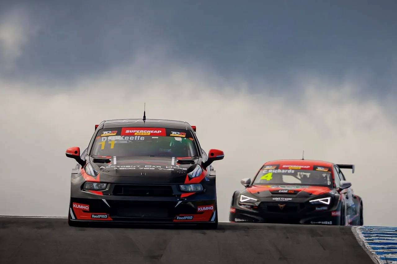 Black number 11 Autoglym Lynk & Co TCR car crests a rise ahead of the number 4 car under a stormy sky