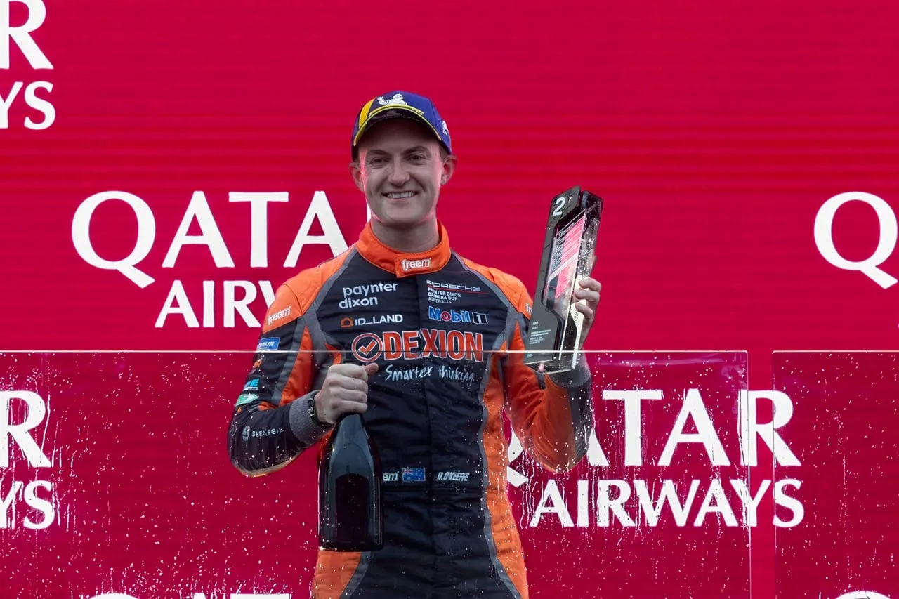 Dylan O’Keeffe on the podium holding a second-place trophy and champagne in front of Qatar Airways signage