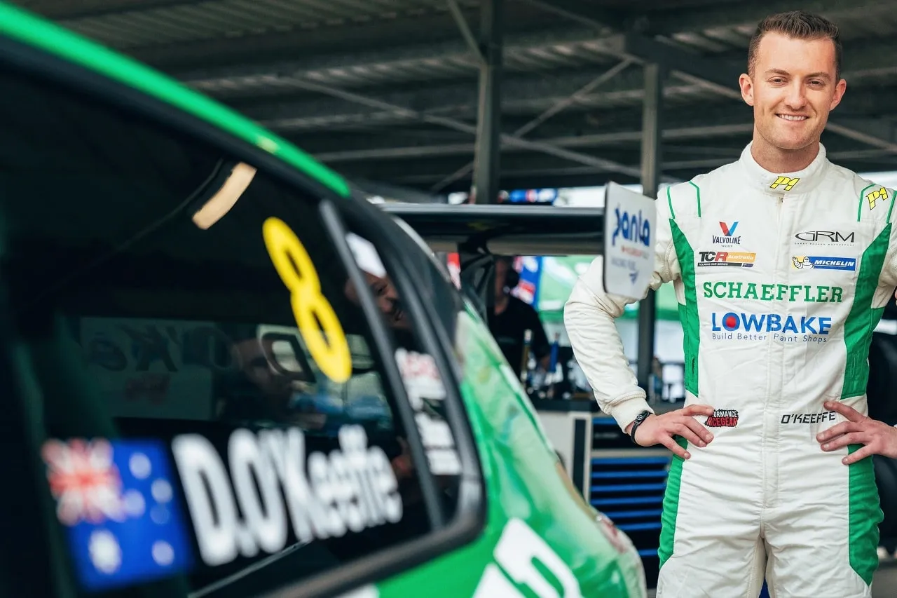 Dylan O’Keeffe smiling in a white Schaeffler race suit beside his #8 Peugeot TCR car
