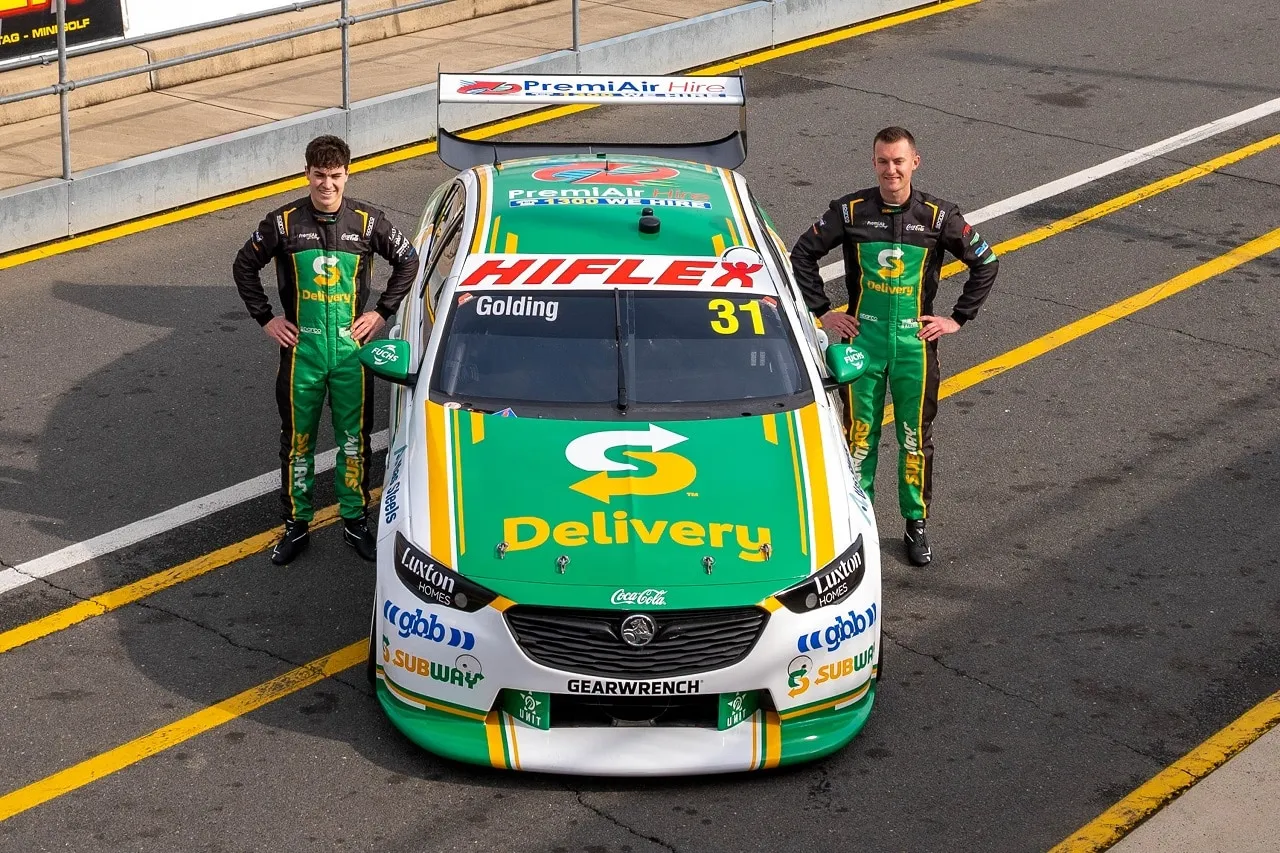 Two drivers in Subway race suits stand either side of the #31 Subway Supercar in pit lane