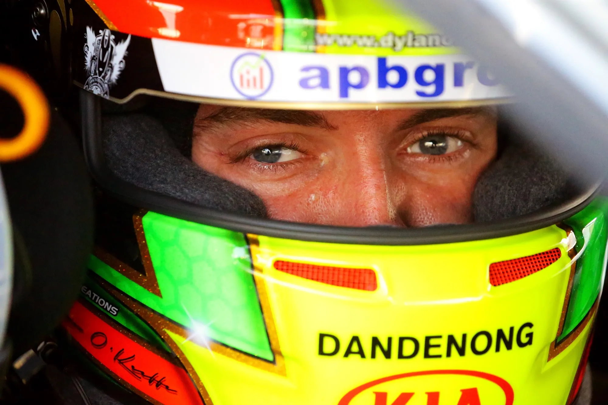 Close-up of Dylan O’Keeffe’s eyes inside his green and yellow helmet, marked Dandenong Kia and apbgroup