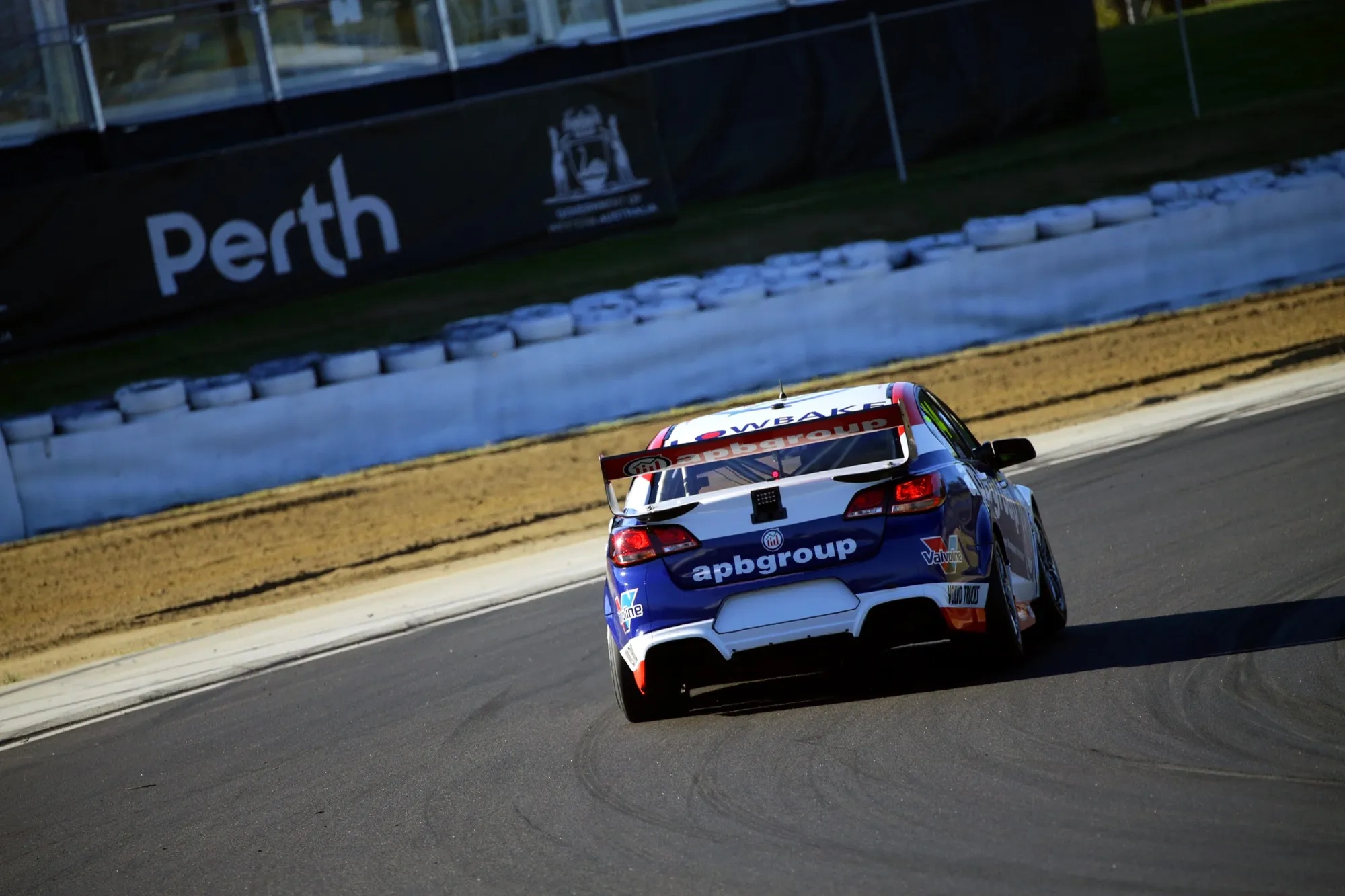 Rear view of the #44 apbgroup Commodore Supercar on track beside a Perth-branded tyre wall